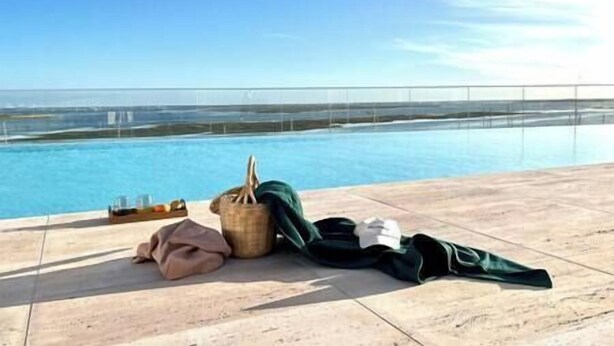 Ein Poolbereich mit freiem Blick auf den Ozean, einem Strandschirm, einem Liegestuhl und einer Strandtasche.