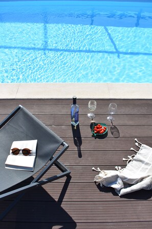 A poolside area with a lounge chair, a bottle, glasses, and a bowl of fruit.