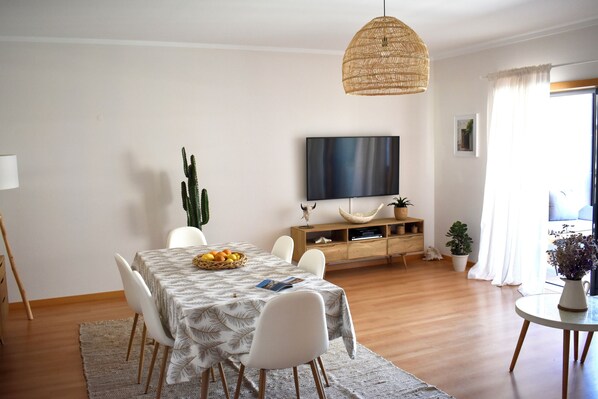 A dining area with a table set for four, a television mounted on the wall, and a large cactus plant.