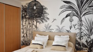 A bedroom with a bed, pillows, a bedside table, and a wall mural. - Luz Marina - Olhão, Algarve (Olhão)