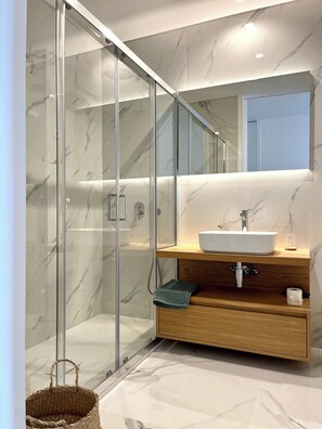 A modern bathroom with a glass shower enclosure, a wooden vanity, and a large mirror above the sink.