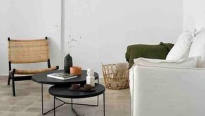 Una sala de estar con una mesa redonda negra, una silla de mimbre, un sofá blanco y una cesta tejida.