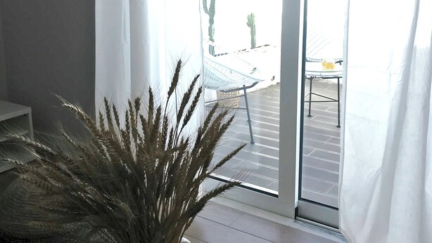 A room with a large window, a potted plant, a white chair, and a table with a book. - Luz Cubo - Olhão, Algarve (Olhão)