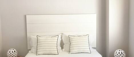 A neatly made bed with two pillows, a bedside table with a decorative item, and a wall-mounted headboard.