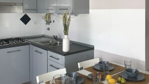 A modern kitchen with grey cabinets, a white countertop, and a dining table set with blue plates and a glass pitcher of orange juice. - Luz Cubo - Olhão, Algarve (Olhão)