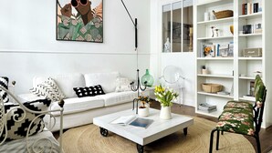 A modern living room with a white sofa, a coffee table with books, a clear chair, and a bookshelf filled with books and decorative items. - Casa Saudade - Olhão, Algarve (Olhão)