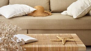 A beige sofa with white cushions, a woven table with a starfish decoration, and a straw hat. - Luz Santana - Olhão, Algarve (Olhão)