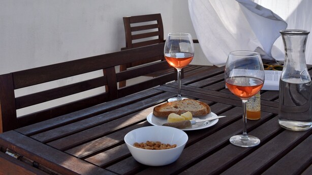 A rooftop terrace with a table set for two, featuring a bottle of water, two glasses of rosé wine, a bowl of snacks, and a plate of bread. - Luz Santana - Olhão, Algarve (Olhão)