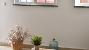 A room with two windows, a woven table, a starfish decoration, a potted plant, a wicker basket, and a blue vase. - Luz Santana - Olhão, Algarve (Olhão)