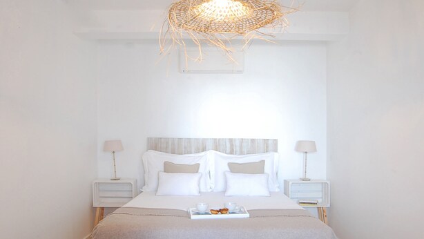A neatly arranged bedroom with a bed centered between two nightstands, each with a lamp. A tray with cups and pastries is on the bed.