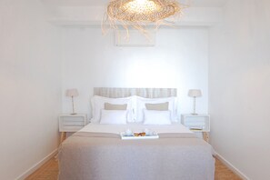 A neatly arranged bedroom with a bed centered between two nightstands, each with a lamp. A tray with cups and pastries is on the bed. - Luz Restauração - Olhão, Algarve (Olhão)