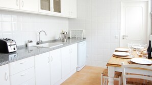 A modern kitchen with white cabinets, a granite countertop, a built-in dishwasher, and a dining area with a wooden table and chairs.