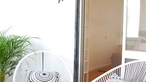 A room with a white chair, a potted plant, and a glass door leading to another room.