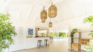 Une pièce lumineuse et spacieuse avec un plafond blanc, une piscine en arrière-plan et un comptoir de bar avec des tabourets.