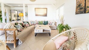 Un salon spacieux comprenant un canapé, une table basse et un fauteuil en osier.