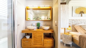 Une salle de bain moderne avec des meubles en bois, un grand miroir et une table de chevet avec une lampe.