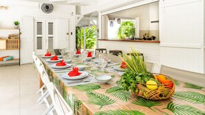 Une longue table à manger, dressée avec des assiettes, des verres et un centre de table composé de légumes et d’herbes fraîches.