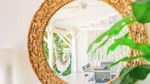A round woven mirror on a wall, a cactus plant, and a glimpse of a room with a white ceiling and a hanging plant.