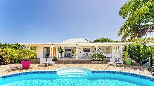 A pool area with a house in the background, surrounded by greenery.