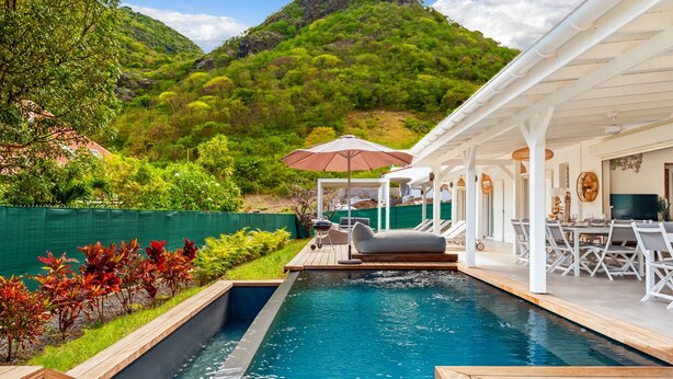 Zona de piscina con vistas a la montaña, mobiliario exterior y un porche cubierto.