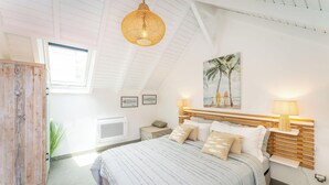 Un dormitorio con una cama, cabecera de madera, una ventana y un cuadro de palmeras.
