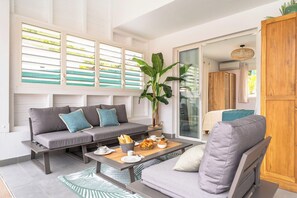 Een moderne woonkamer met een grijze bank, een houten salontafel en een grote plant.