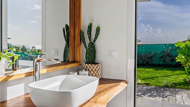 Un baño moderno con un lavamanos grande blanco, encimera de madera y vistas a un jardín verde a través de una puerta de cristal.
