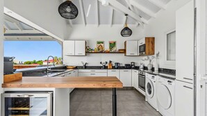 Una cocina moderna con armarios blancos, encimera de madera y lavadora integrada.