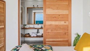 Un dormitorio con un armario de madera, una cama con colcha estampada y una planta en la mesita de noche, con vista al mar a través de una ventana.