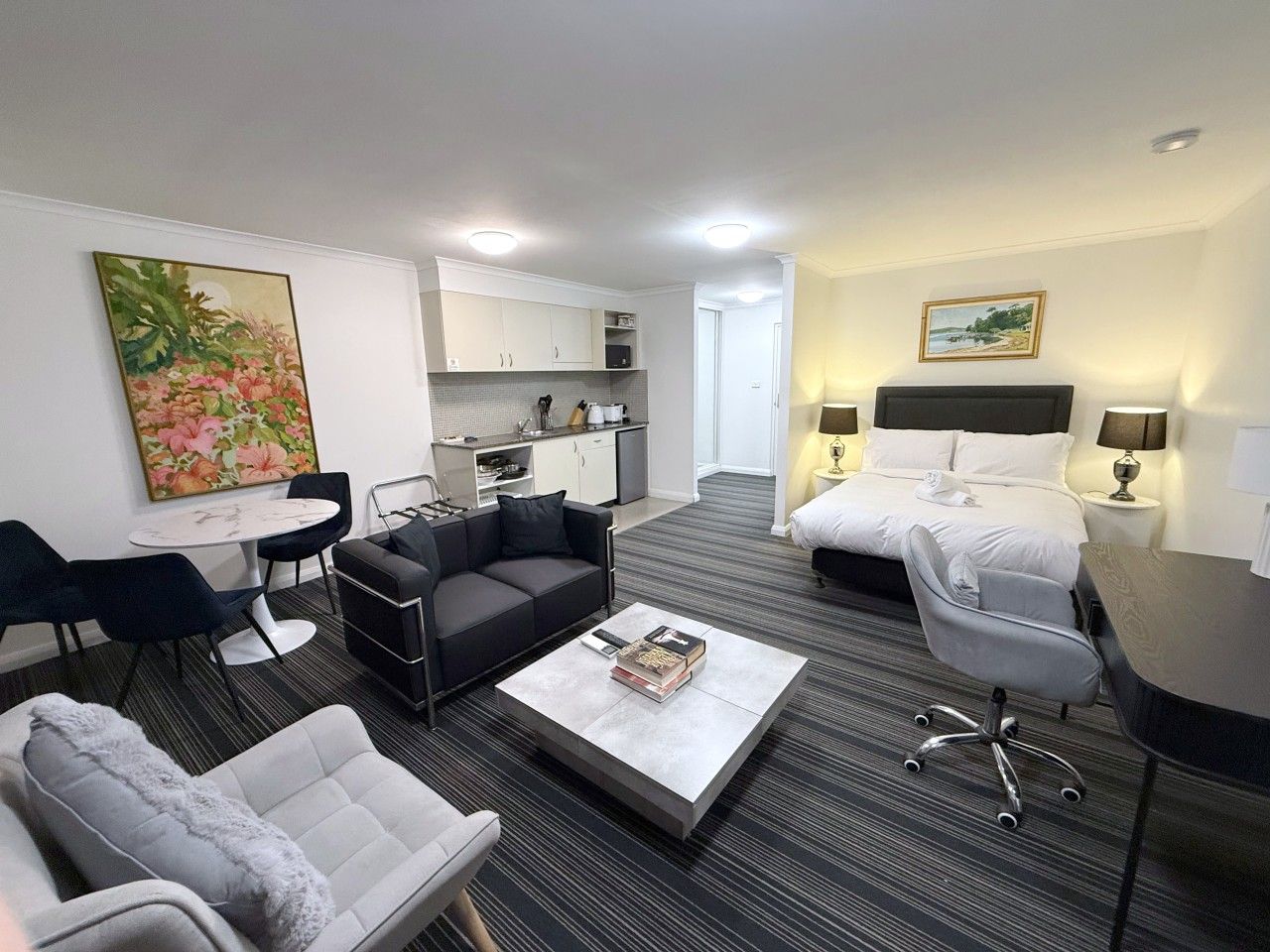 Ein Hotelzimmer mit Wohnbereich, separatem Essbereich, einer Küchenzeile und einem Schlafzimmer mit Bett und Nachttischen.