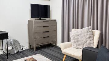 Uma sala de estar moderna com um sofá, uma mesa de centro com livros e um controle remoto, uma TV sobre um suporte, um aparador e uma janela grande com cortinas.