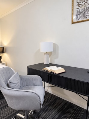 A modern hotel room with a grey upholstered chair, a black desk with a lamp, and a framed artwork on the wall. - Spacious Studio Apartment in CBD Wi-Fi Included (Sydney)