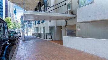 A covered pedestrian walkway with parked cars on one side and a building with a white facade and large windows.