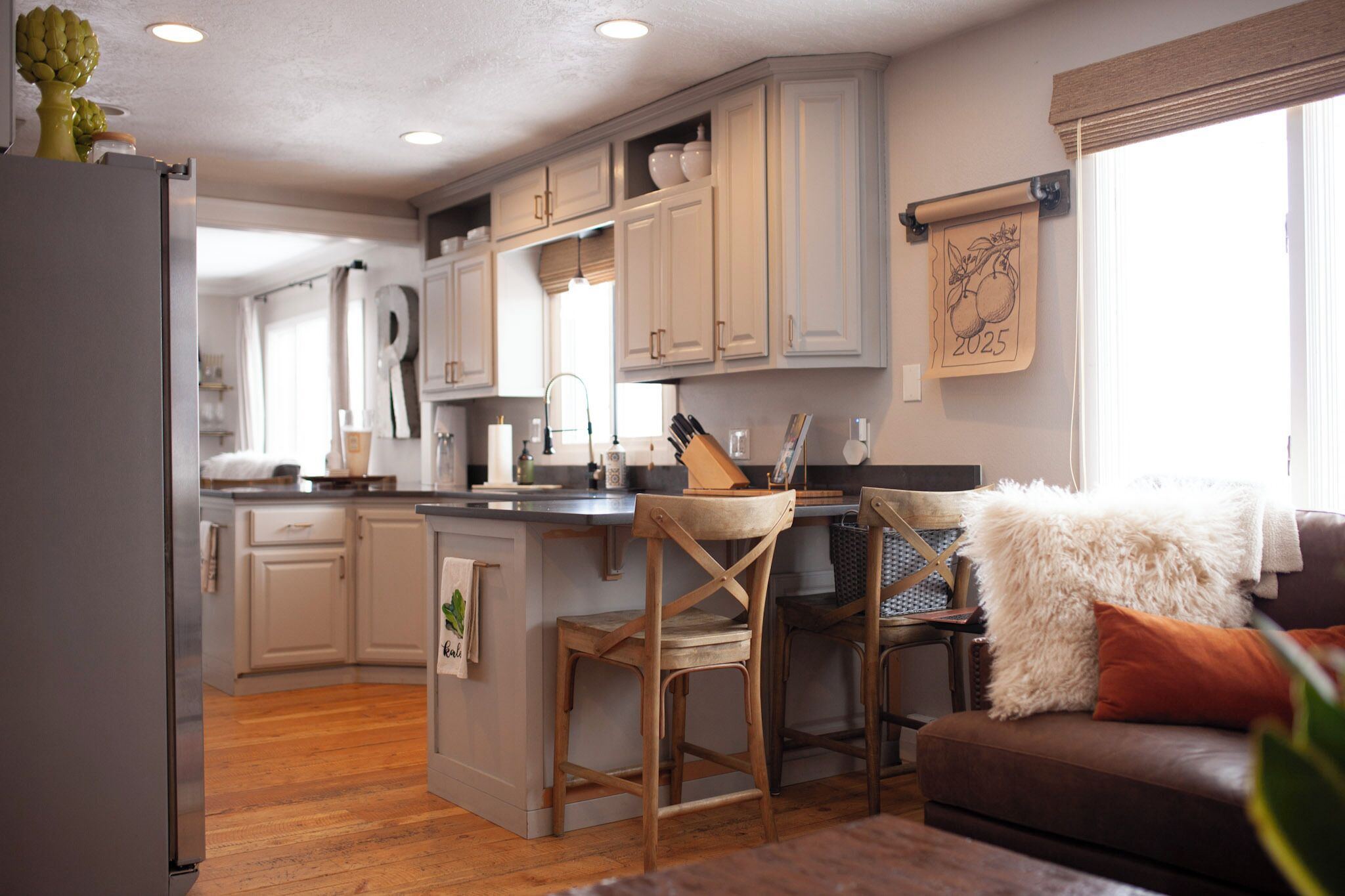 A modern kitchen with white cabinets, a wooden island, and a dining area with a brown leather couch and fluffy white pillows.