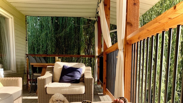 A covered porch with a cushioned seating area, a small dog, and a person's feet resting on a cushion. - Charming 4 bedroom home in beautiful Missoula w/ great proximity to all the fun! (Missoula)
