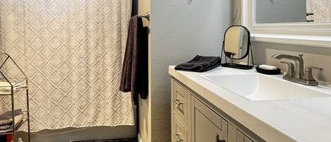 A bathroom with a large mirror, a sink, and a towel rack.