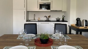 Een moderne keuken met witte kastjes, een roestvrijstalen oven en een zwart aanrecht. Er staat een eettafel met stoelen en een rode placemat met een potplant.