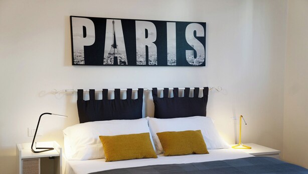 A neatly arranged bedroom with a bed, two bedside lamps, a nightstand, and a wall-mounted sign that reads "PARIS".