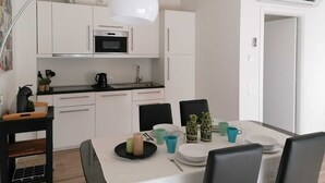 A modern kitchen with white cabinets, a black countertop, and a built-in oven. There is a dining table with chairs, a white pendant light, and a small plant on the table. - Eco Apartment View By Case al Lago (Peschiera del Garda)