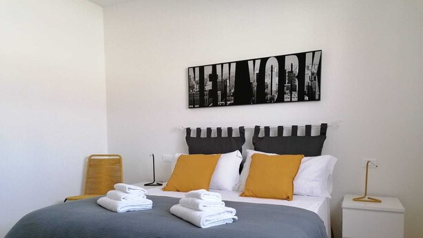 A neatly made bed with a grey and black bedspread, white pillows, and a black and white cityscape artwork above it. - Eco Apartment View By Case al Lago (Peschiera del Garda)