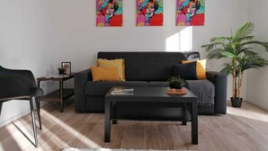 A modern living room with a black sofa, a coffee table, and three colorful paintings on the wall. - Eco Apartment View By Case al Lago (Peschiera del Garda)