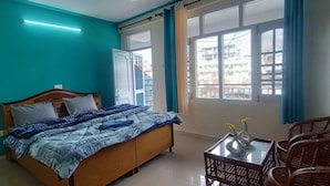 A bedroom with a bed, a table with a vase, and a window with curtains. - Check-in & Chill (Dharamshala)