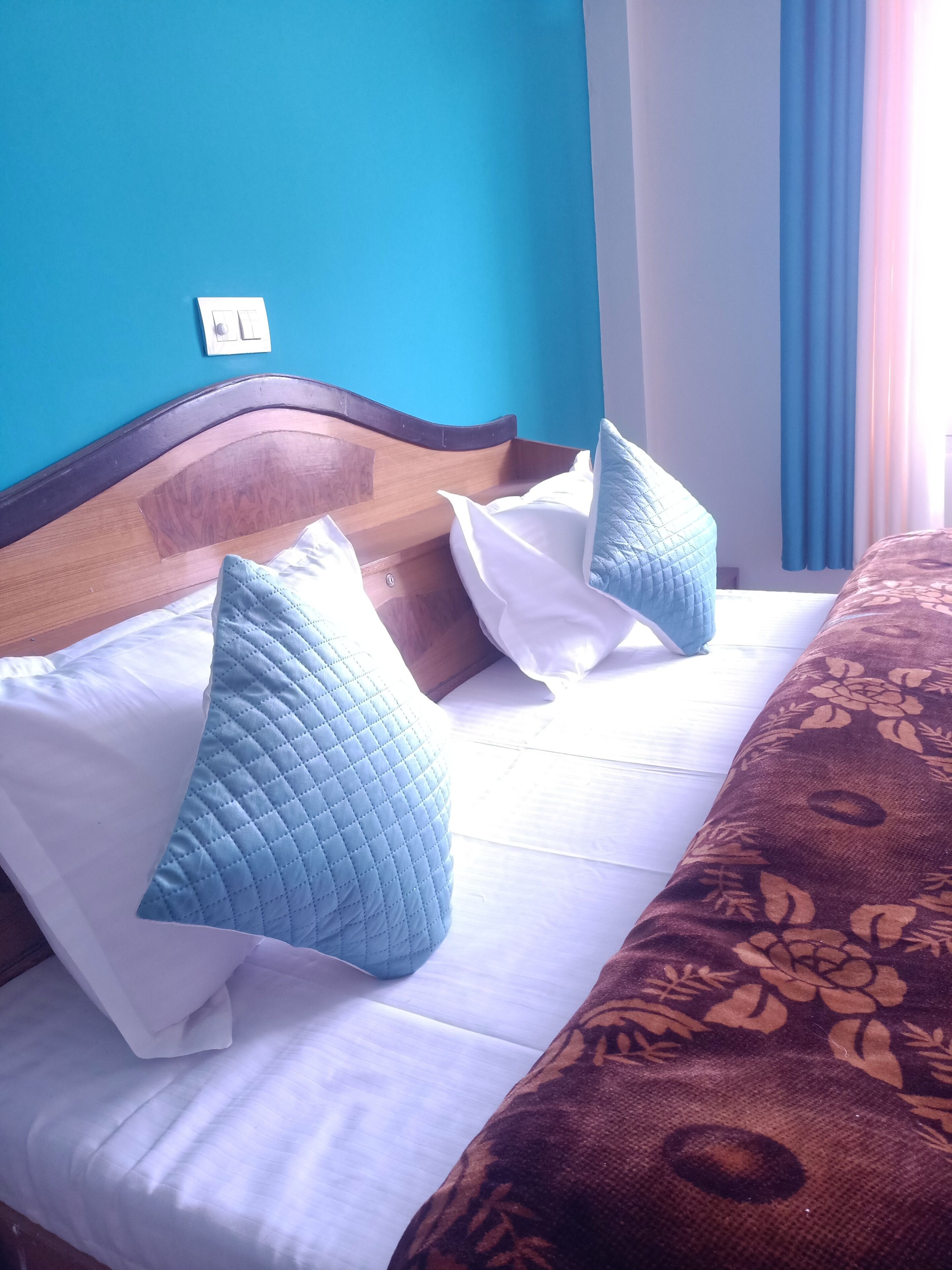 A bed with a wooden headboard, white and blue pillows, and a brown patterned bedspread.