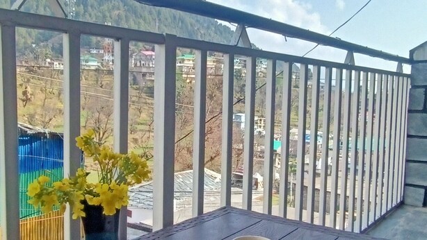 A balcony with a wooden floor, a blue vase with yellow flowers, and two beige mugs. - Check-in & Chill (Dharamshala)
