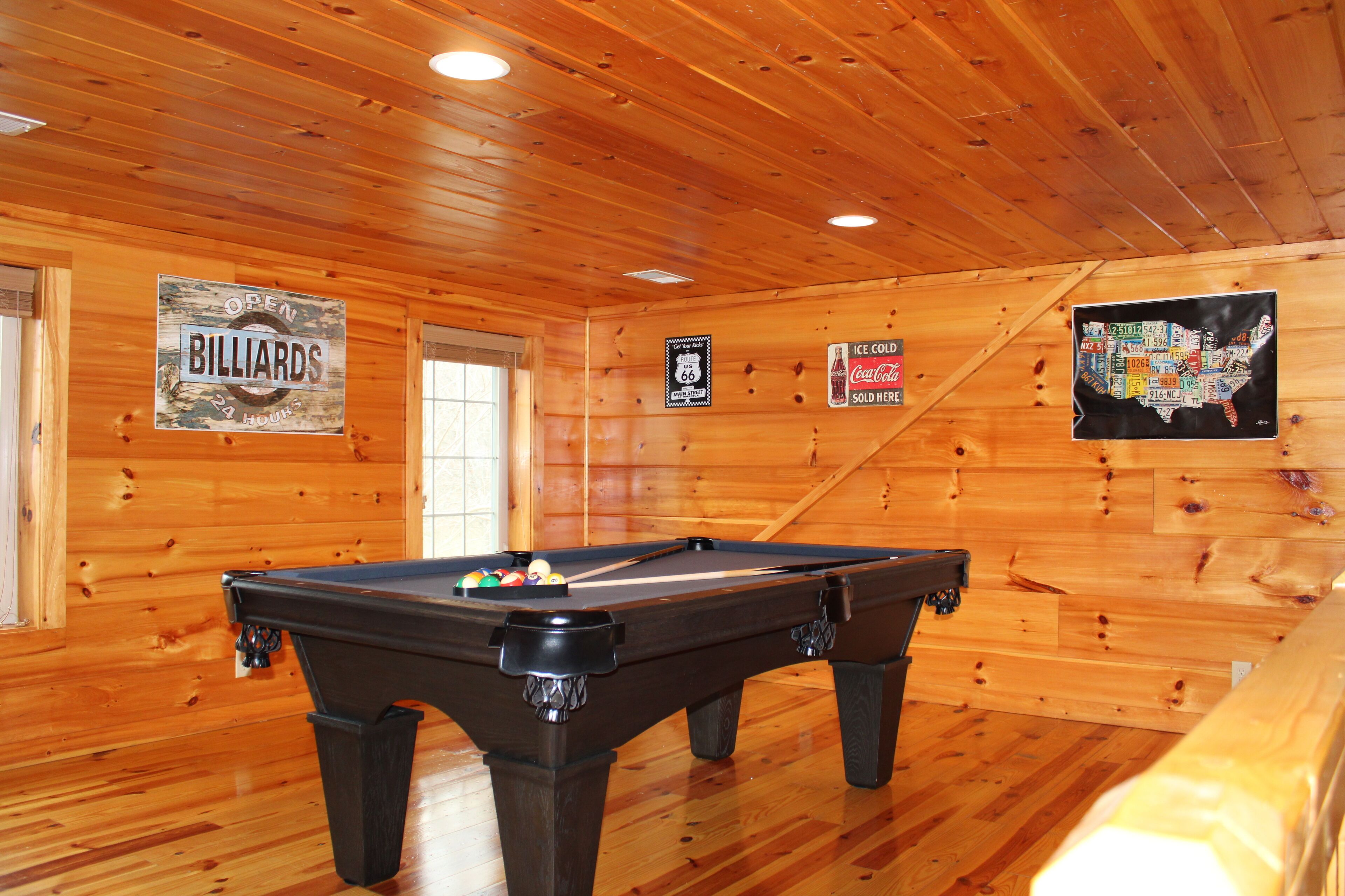 A pool table in a wooden room with signs for billiards, a Coca-Cola sign, and a map of the USA.