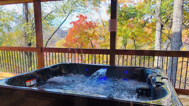 A hot tub with a wooden deck and a view of autumn trees. - Gatlinburg, Charming Cabin Hearth of Nature With Pool Table, Fireplace, Hot Tub (Sevierville)