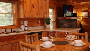 A wooden cabin interior with a kitchen, dining area, and a TV mounted on the wall. - Gatlinburg, Charming Cabin Hearth of Nature With Pool Table, Fireplace, Hot Tub (Sevierville)