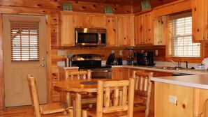 A wooden cabin-style kitchen with a central island, wooden chairs, a microwave, a stove, and a sink. - Gatlinburg, Charming Cabin Hearth of Nature With Pool Table, Fireplace, Hot Tub (Sevierville)
