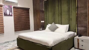 A modern bedroom with a green upholstered headboard, a white bedspread, and a marble-patterned rug.
