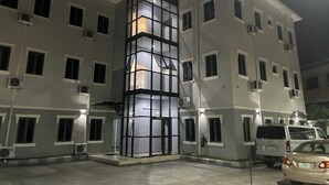 En byggnad med flera våningar, med en central konstruktion av glasblock, luftkonditioneringsanläggningar och en parkeringsplats med bilar.
